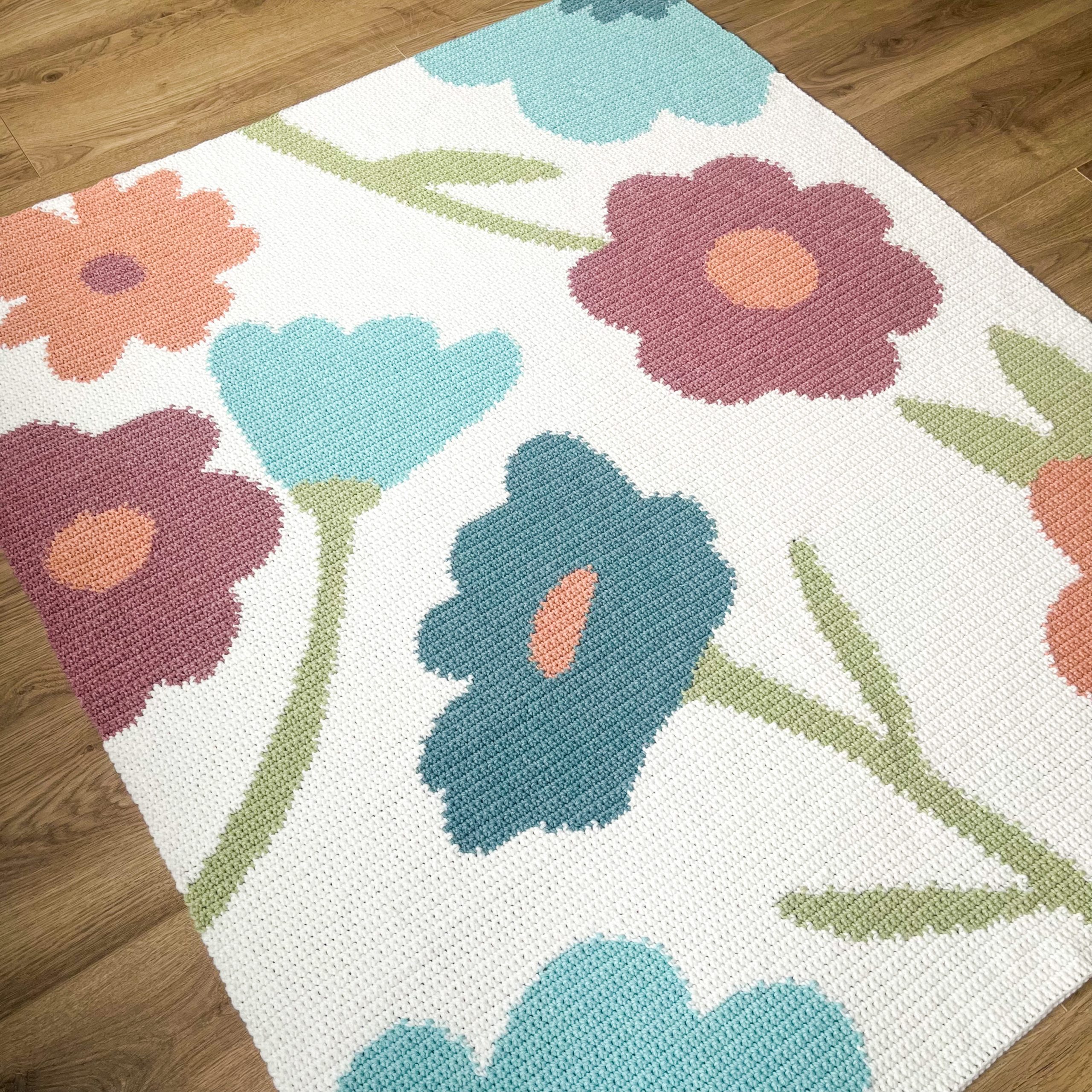 IMG_8757_jpg-scaled White woven rug with large abstract flowers in teal, coral, and pink on a wooden floor.