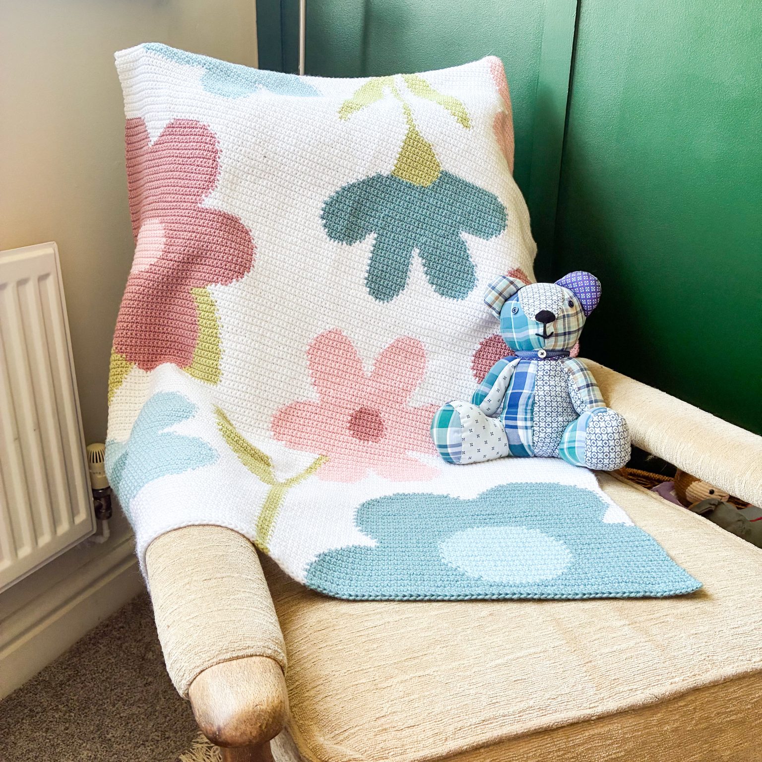 crochet-flower-blanket-for-baby-1536x1536 Beige upholstered armchair with a pastel floral crocheted blanket and a patchwork teddy bear on the seat.