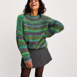 Woman laughing in a thick multicolor knit sweater and gray pleated mini skirt, standing against a light background.