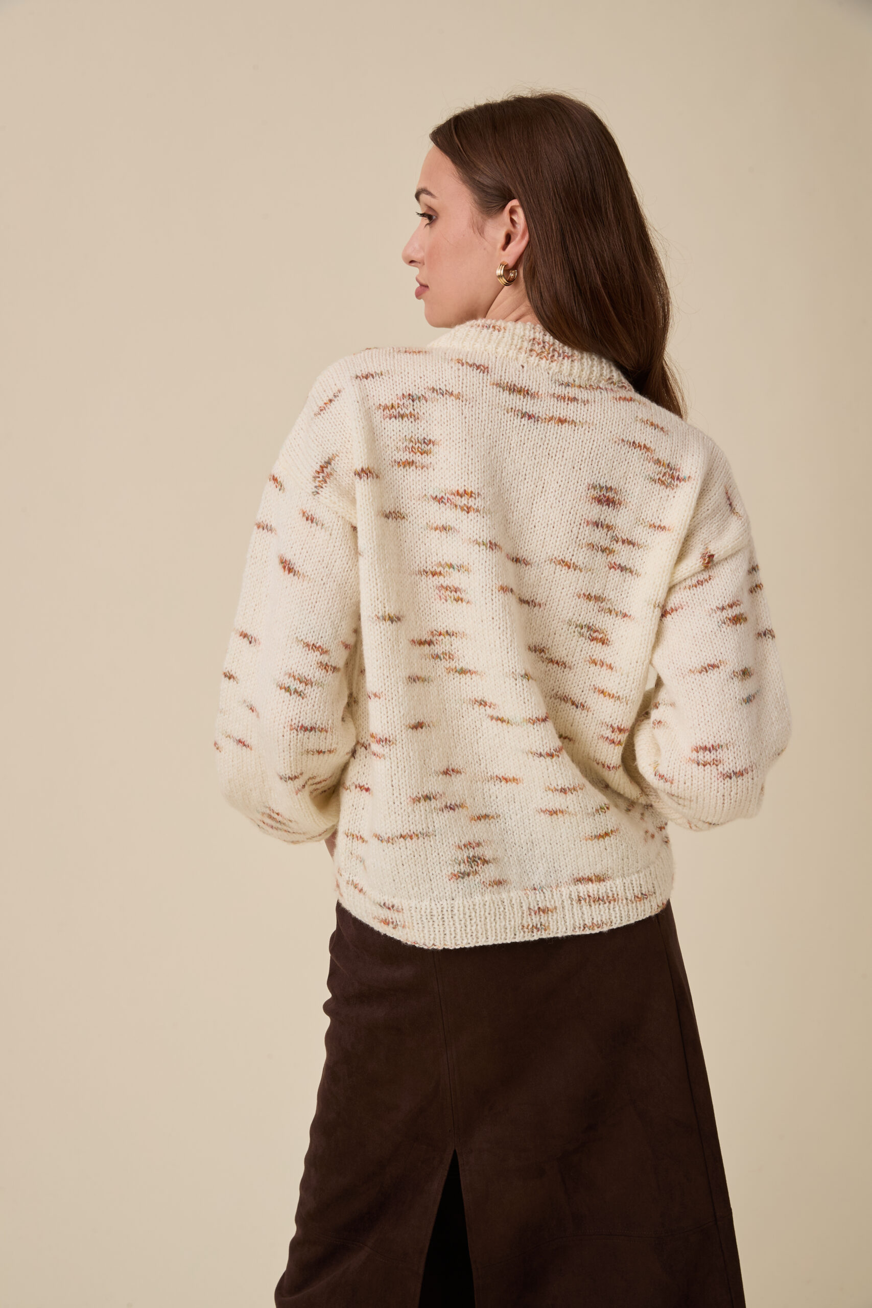 10958 Bright Sparks Sweater img3 Back view of a woman wearing a cream knit sweater with brown flecks and a dark brown skirt against a beige backdrop.