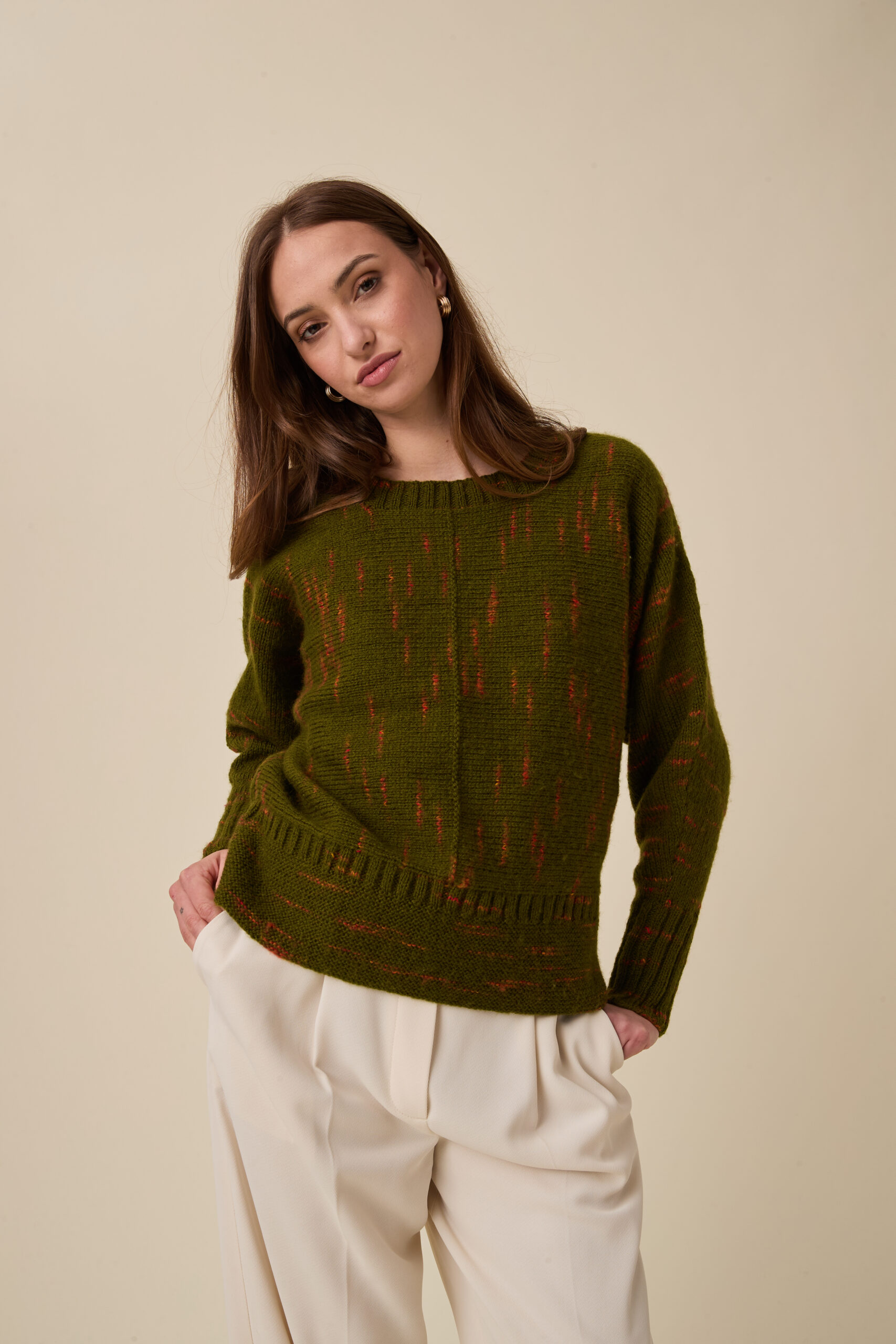 10963 Glimmer Sideways Sweater img2 Woman with brown hair wearing an olive-green knit sweater with red specks, posing against a beige background.