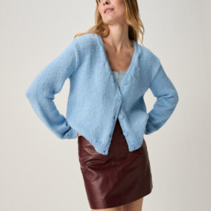 Woman posing in a light blue knitted cardigan over a pale top, burgundy leather skirt, looking to her left with hands on hips. 10967 Stem V Neck Cardigan img1