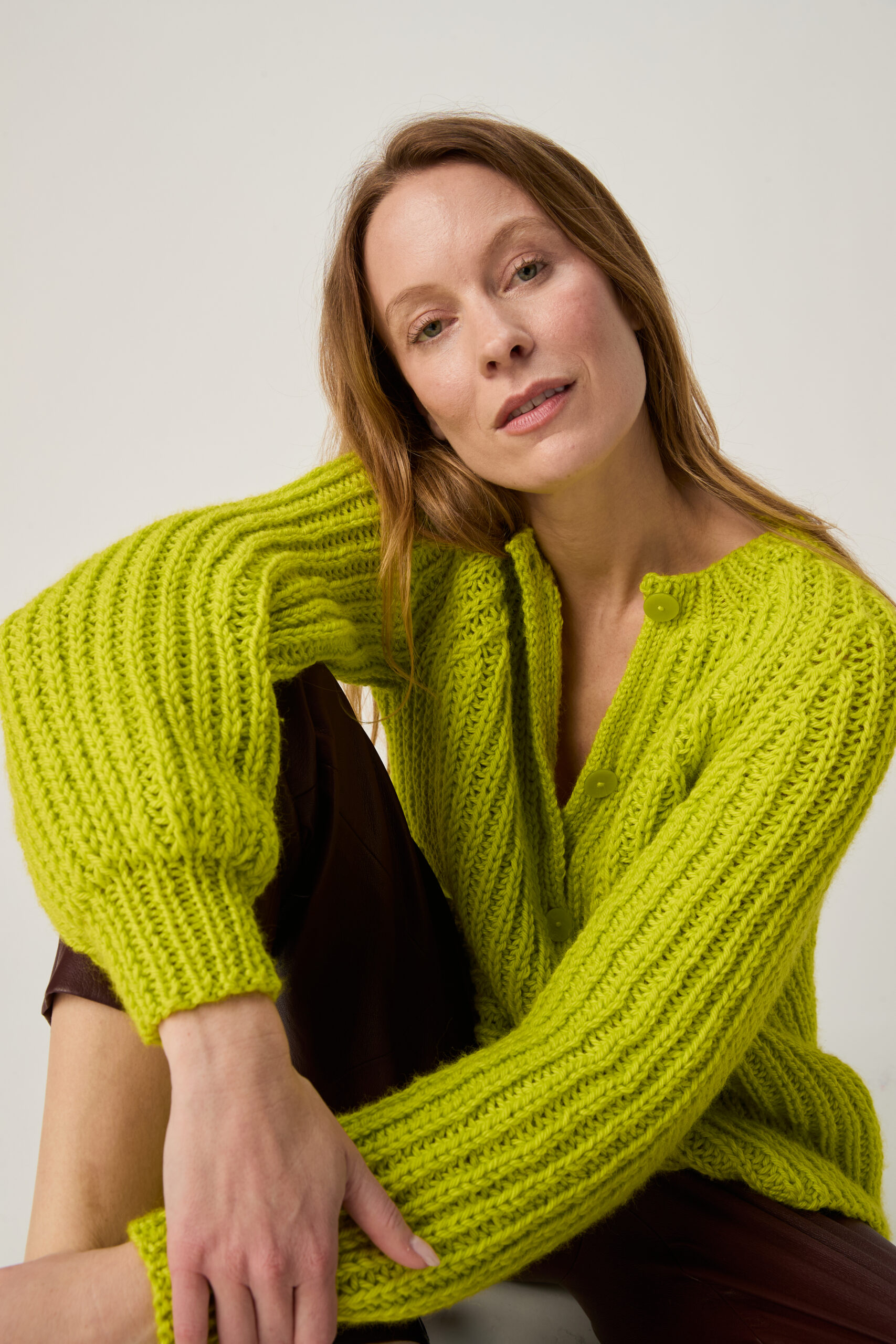 10971 Cultivate Rib Cardigan img2 Woman with long light brown hair wearing a neon green chunky knit sweater, resting her head on her shoulder.