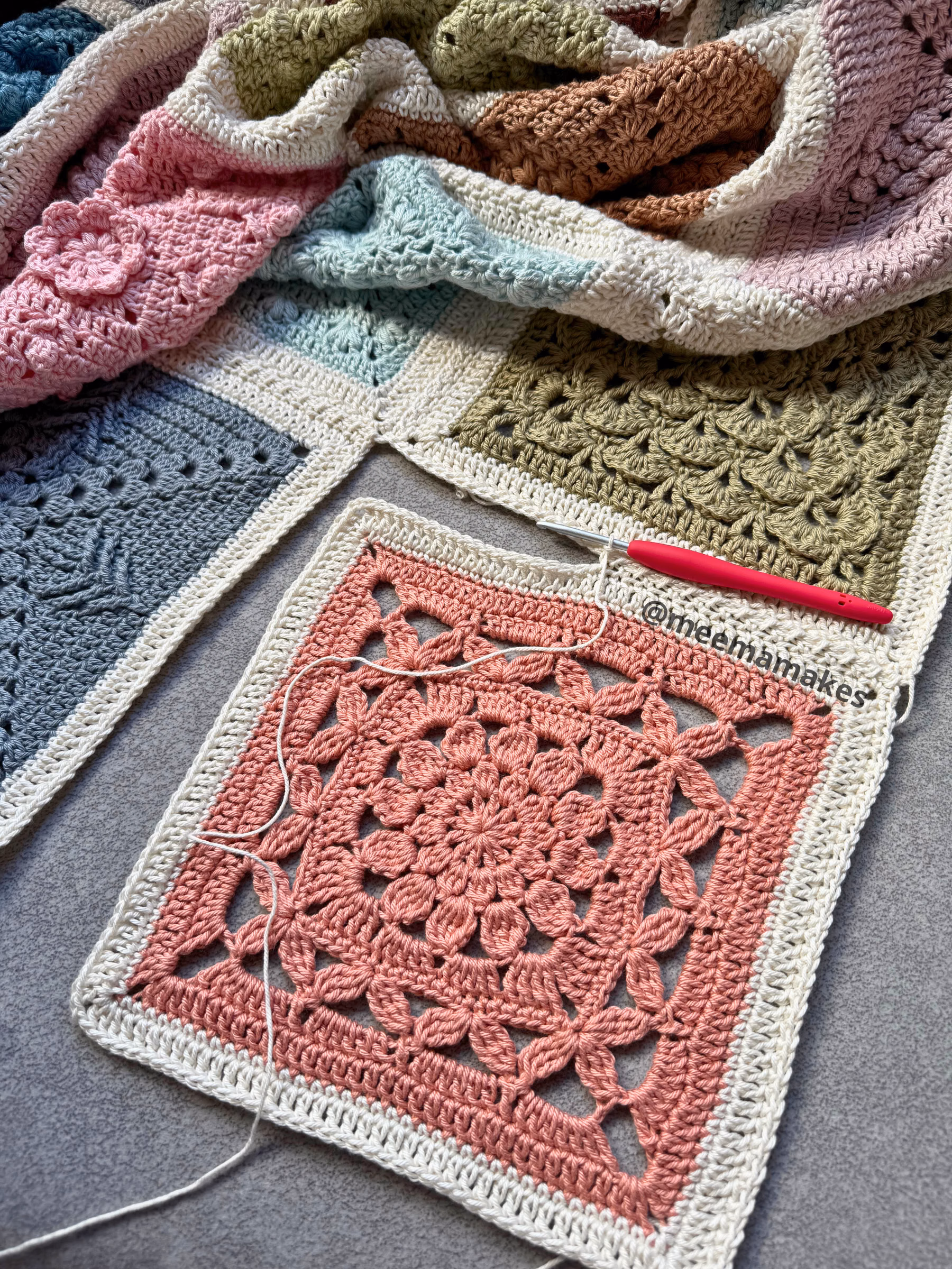 8c09816f-af49-43b8-99eb-a1a101a5571c Layered pastel crocheted blankets with striped borders on a gray surface, a pink crochet hook resting nearby