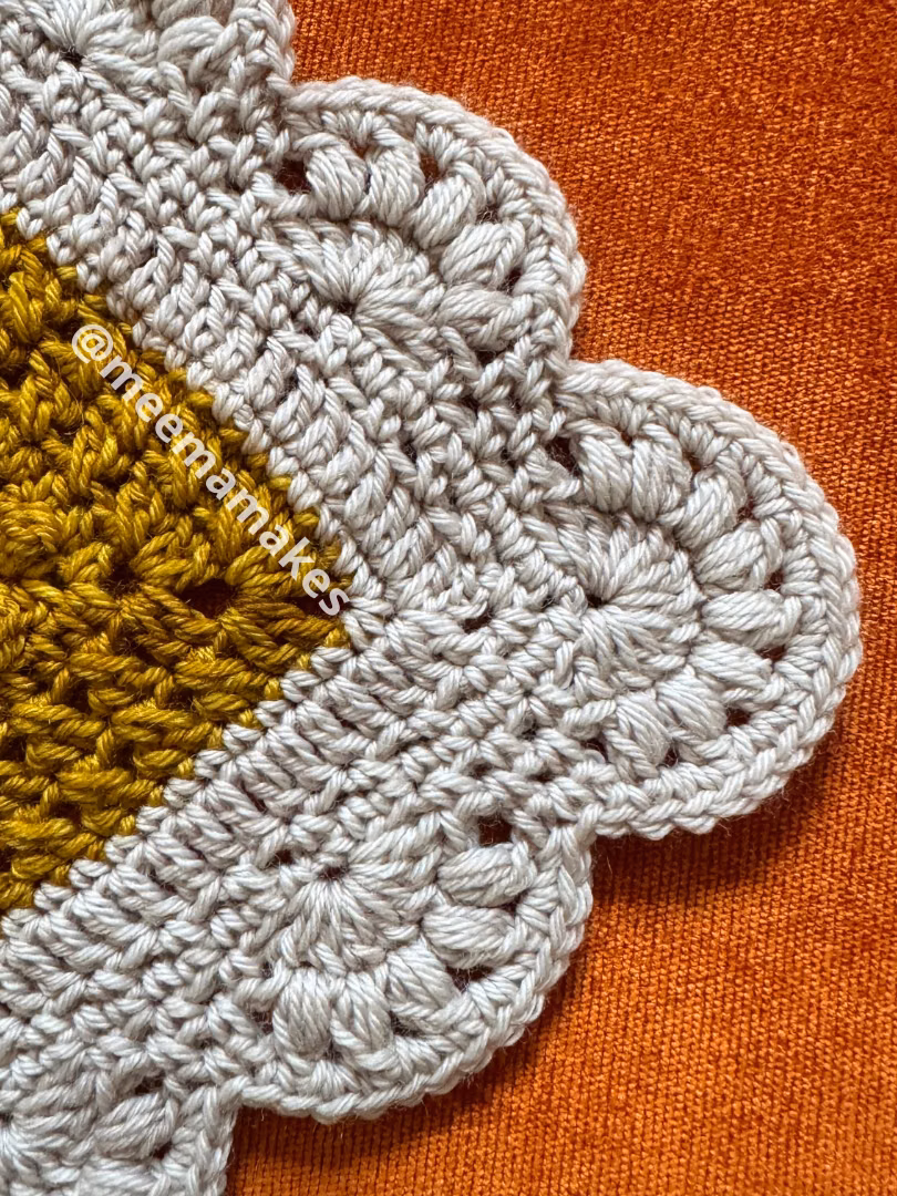 ca657a8b-3cd8-4872-8713-af258ccfc9e2 Crocheted doily with a mustard-yellow center and light gray outer lace set on an orange fabric background.