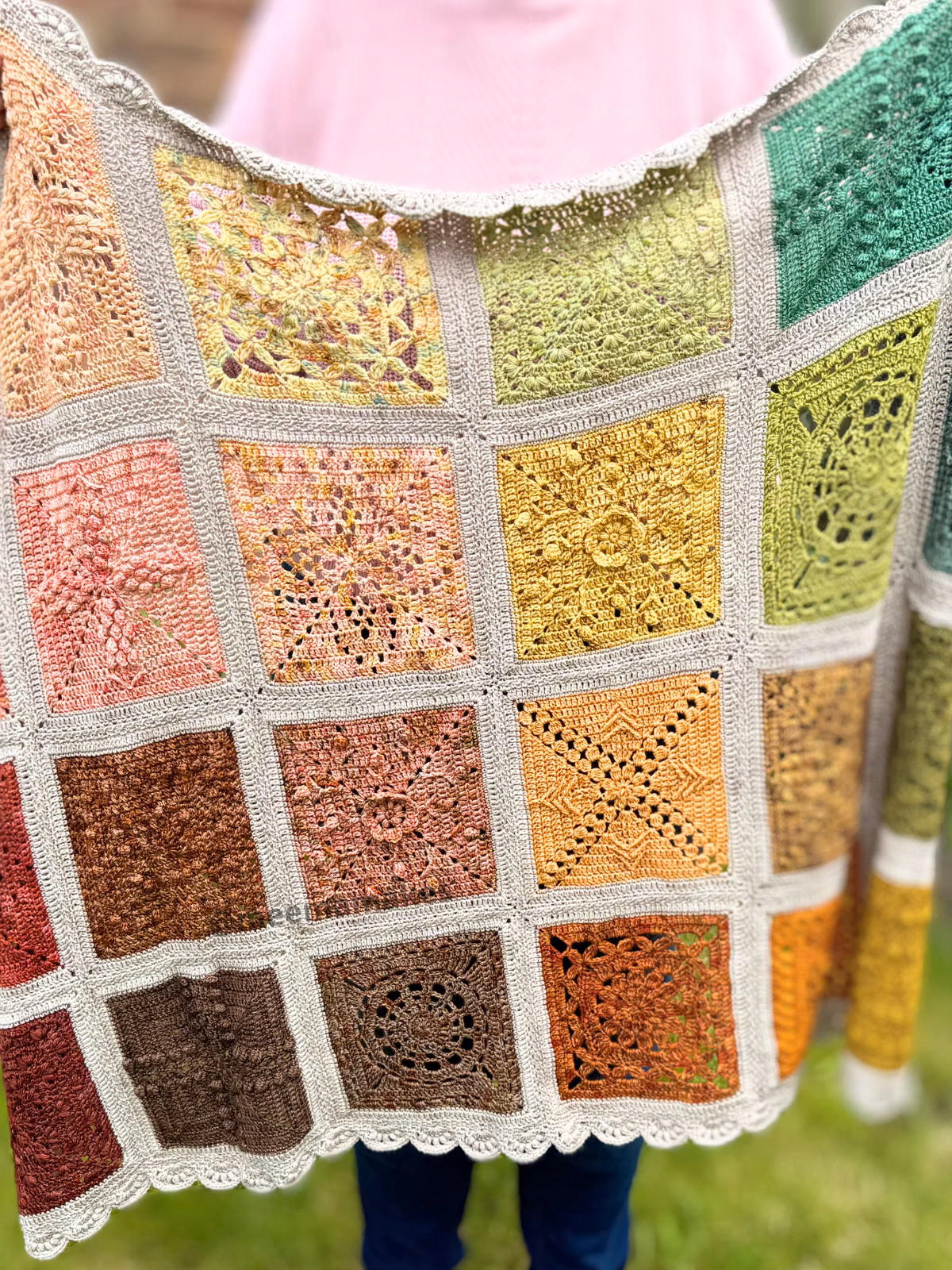 Crocheted shawl made of multicolored granny-square patches with gray borders, draped over a person wearing pink.